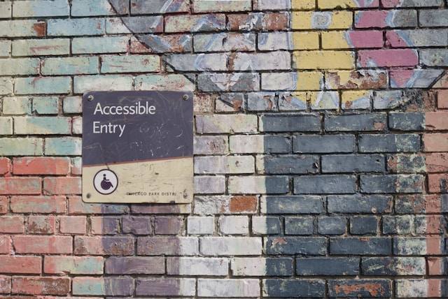 Photo of a brick wall with an accessibility symbol on a sign that has the words accessible entry
