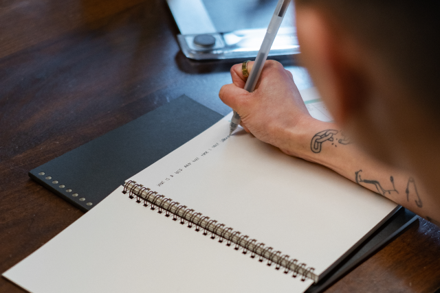 Photograph of a non-binary person writing in a notebook