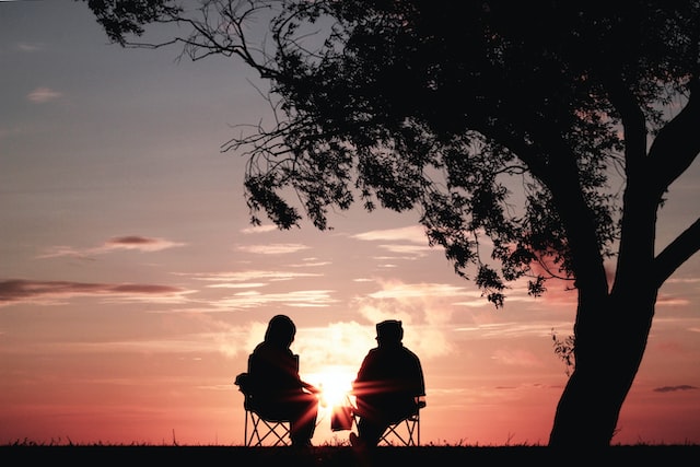 2 people sitting and talking outside as the sun sets