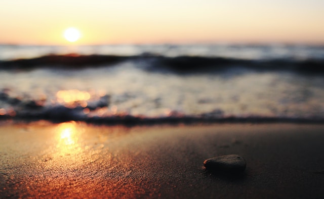 photo of pebble on a beach with the ocean out of focus behind with the sun rising