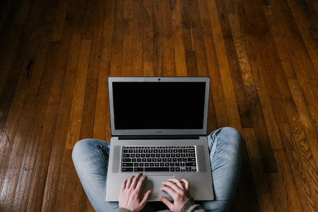 person sitting on the floor in blue jeans with a laptop on their lap