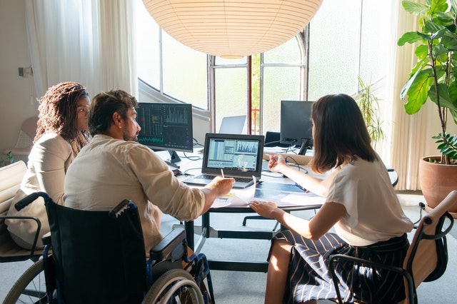 three people sitting at a desk discussing, one person in a wheelchair
