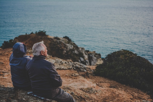 photo of 2 older people sitting on a bench looking at the ocean