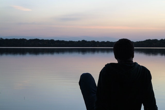 photo of the back of a man facing a lake with the sunsetting