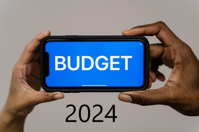photo of a person's hands holding a mobile phone with the word budget on the phone and the date 2024 at the bottom of the photo